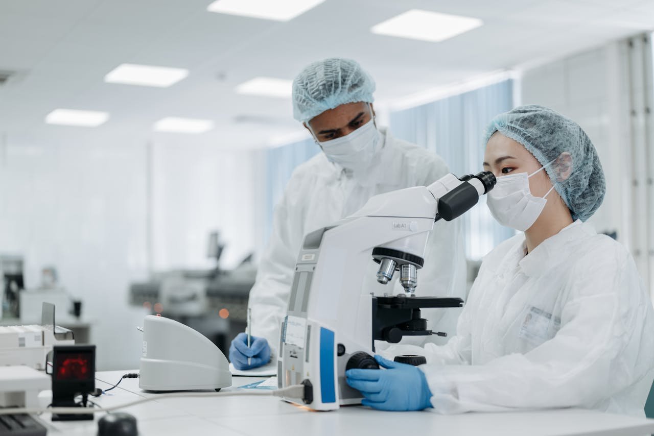 Woman in White Protective Suit Wearing  White Face Mask Looking Through the Microscope